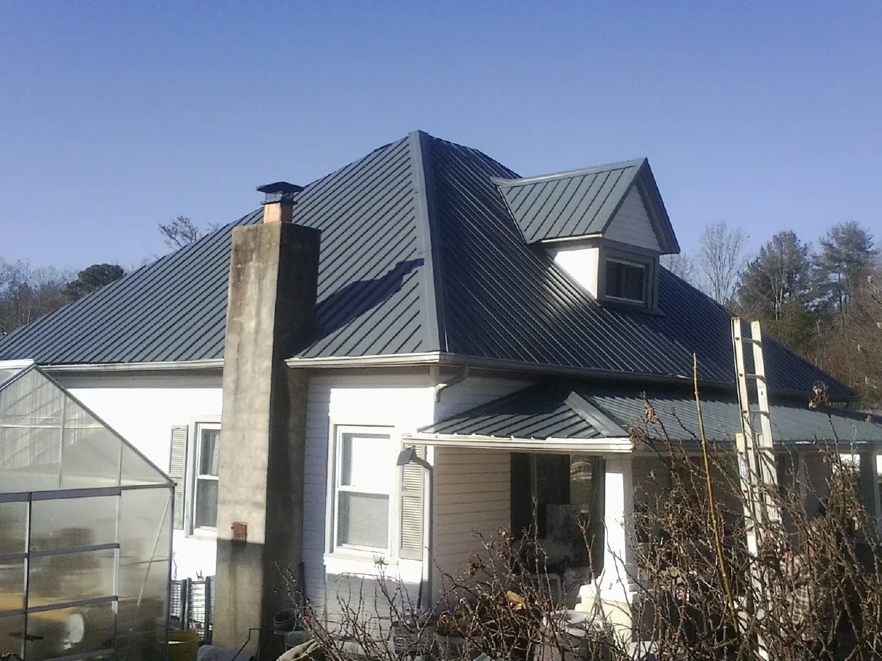 Dark blue standing seam metal roof on a white farmhouse with dormer — Slate & Tile Roof Repair by Roofing Brothers in Adamsburg