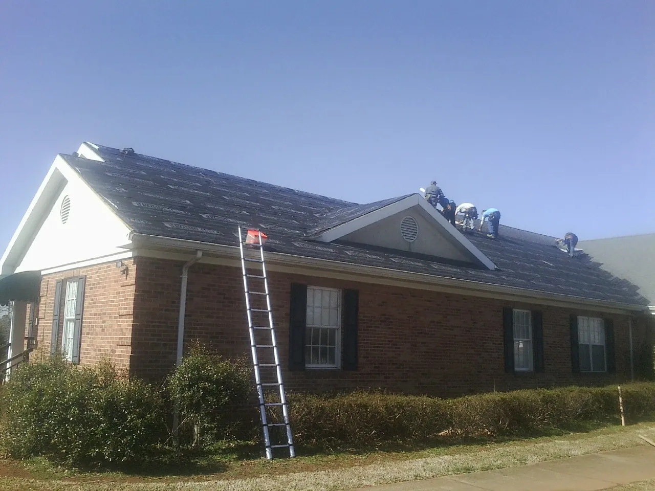 Crew tearing shingles off a brick ranch roof with a ladder set — Metal Roof Repair work by our crew in Adamsburg