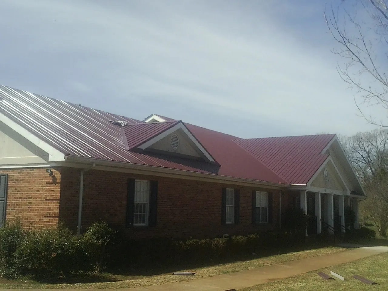 Red metal roof with gabled entries on a long brick building, from a Hail Damage Roof Repair job in Adamsburg