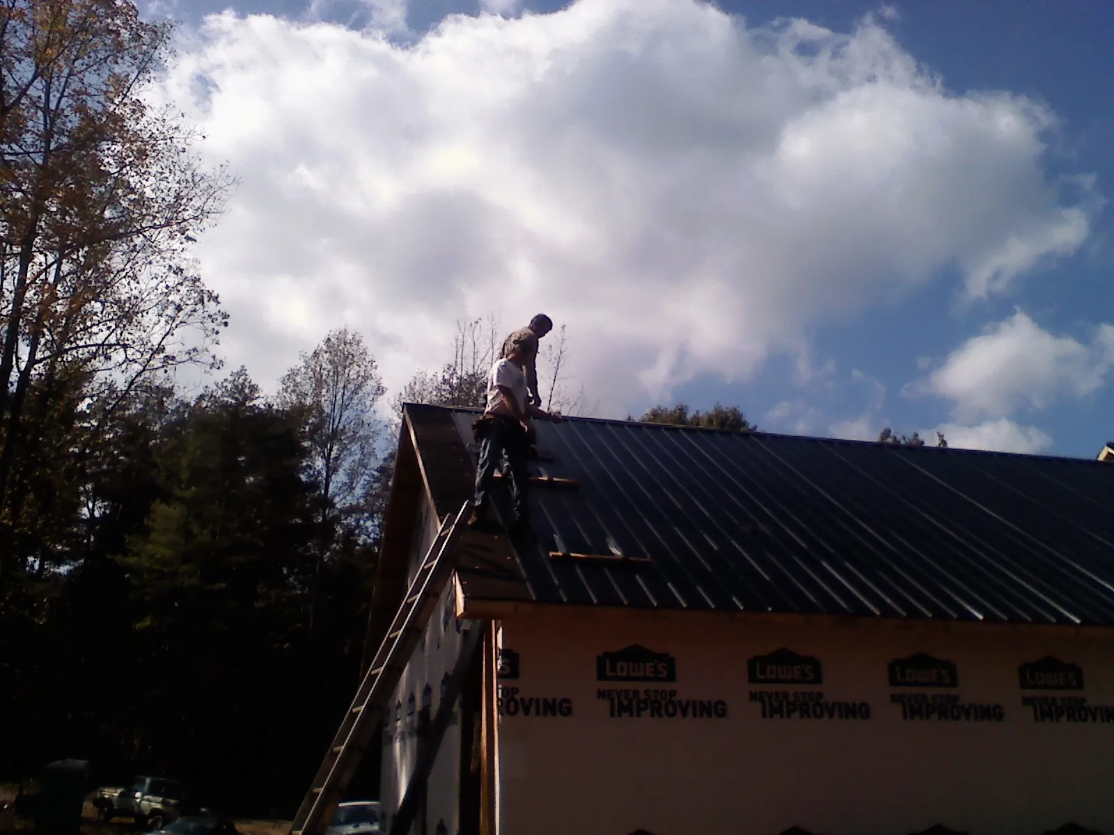 Roofer fastening dark metal panels high against a cloudy sky, from a Roof Inspection job in Adamsburg