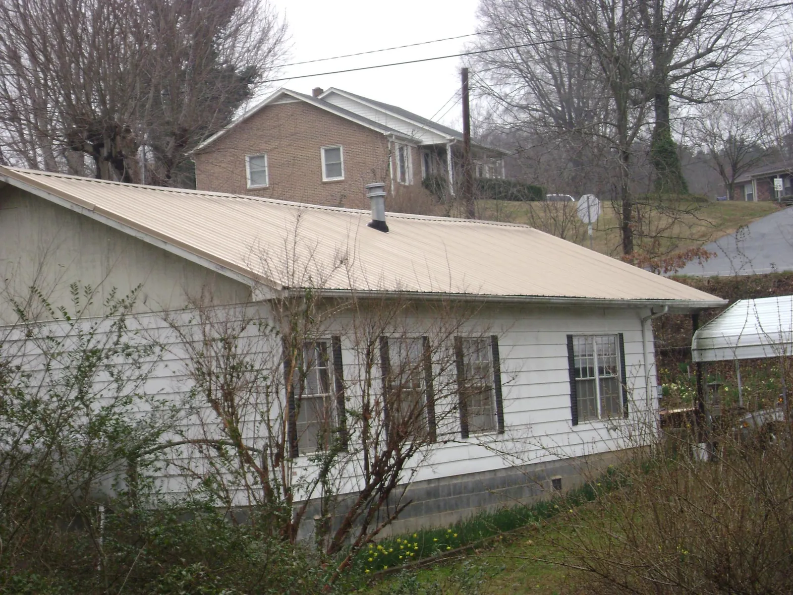 Tan metal roof on a white sided house set into a hillside — Commercial Roofing by Roofing Brothers in Adamsburg