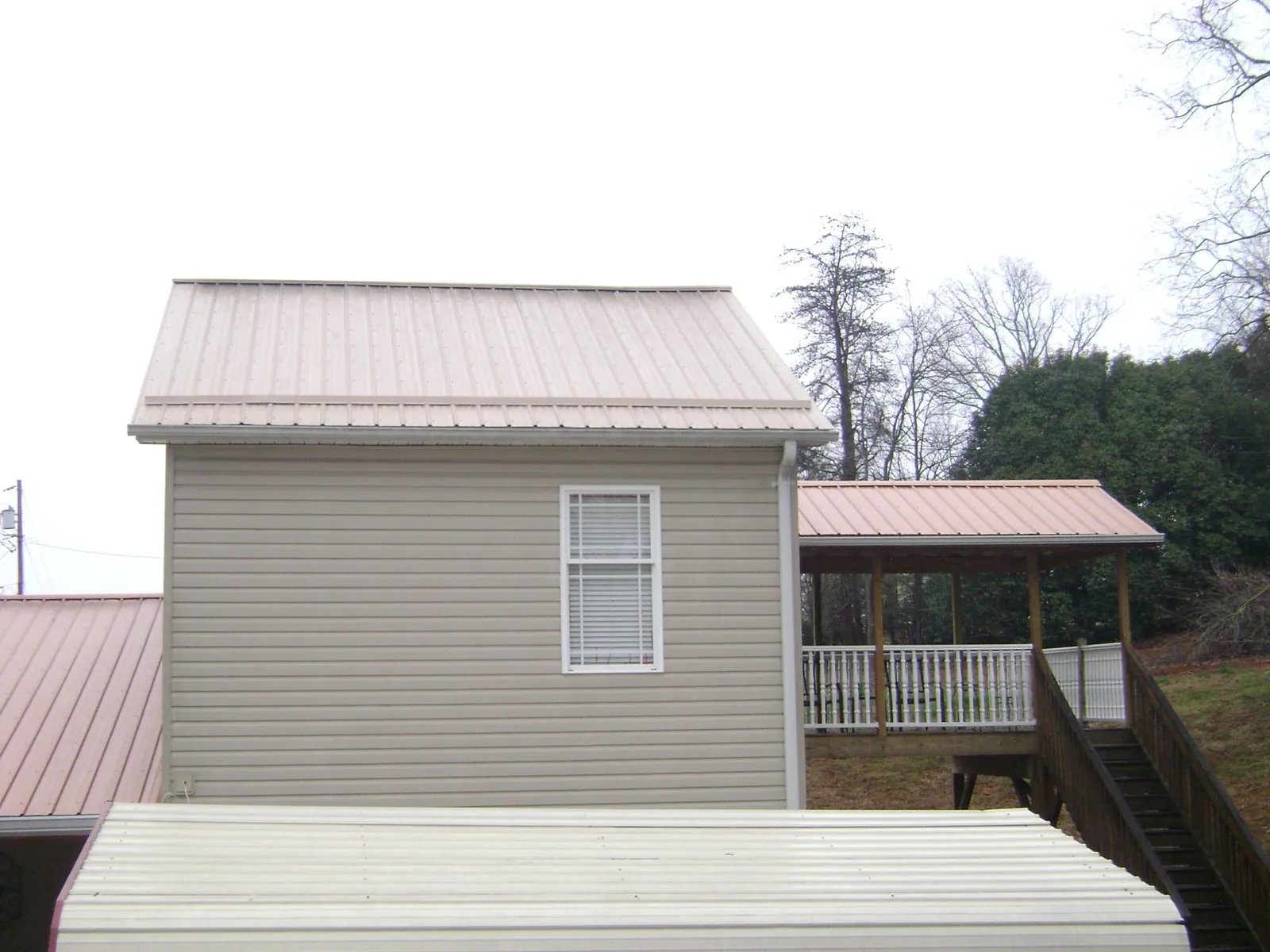 Tan metal roofs on a two story addition and attached porch, from a Roof Replacement job in Adamsburg